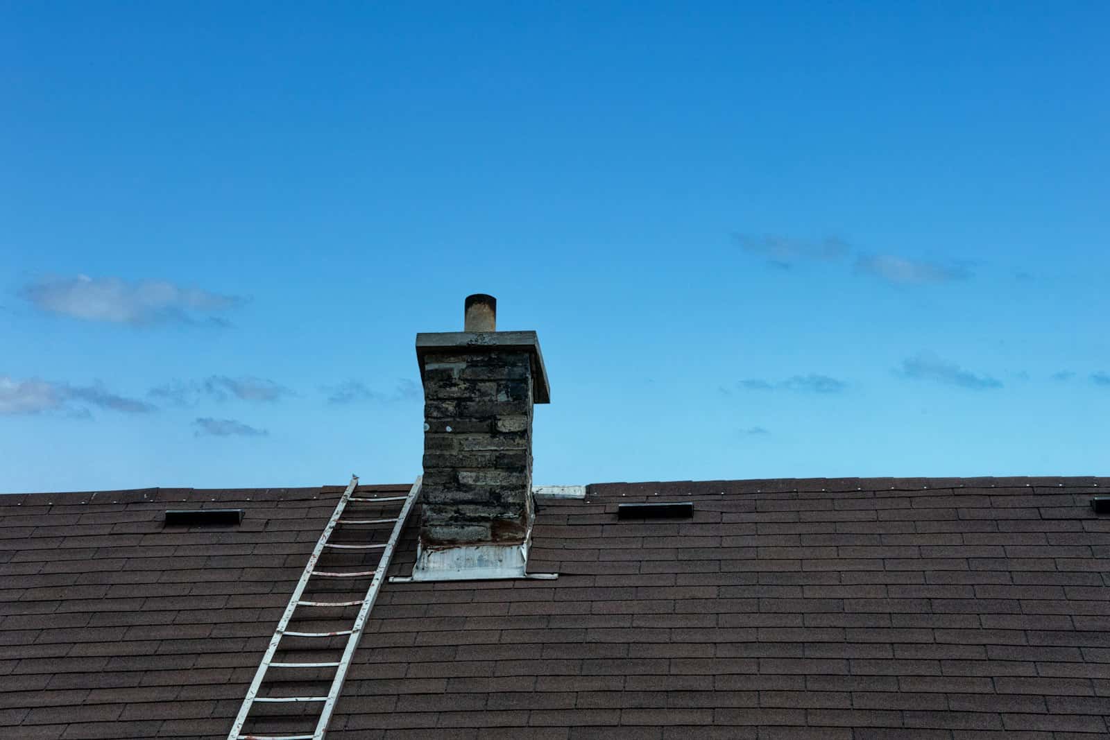 Stone chimney on a shingle roof with a ladder for repair access